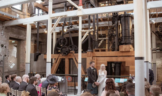 a bride and groom standing in front of the old jute mill at Verdant Works in Dundee during a wedding ceremony as guests seated in rows look on 