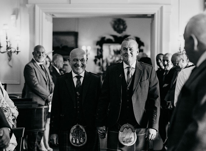 two smiling grooms walking down an aisle while holding hands