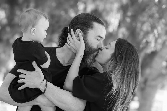 A man and woman kiss while the man holds a baby in his arms