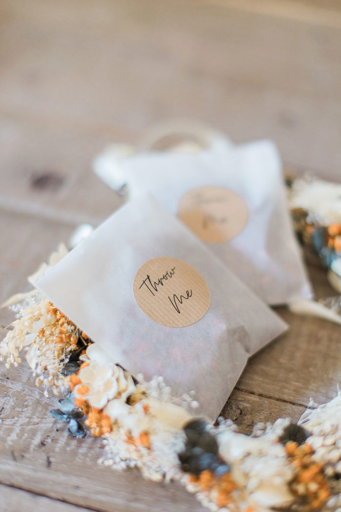 white paper bags with brown sticker that reads 'throw me' and dried floral crown sitting on a wooden surface