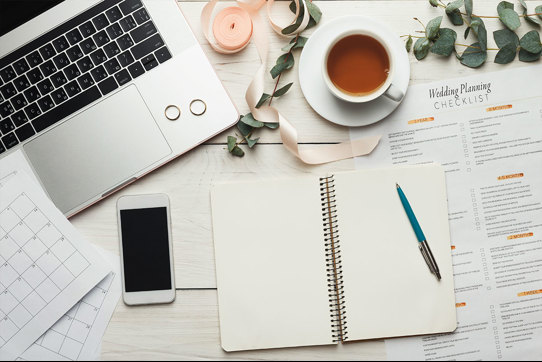 books phone and notepad strewn across desk with laptop