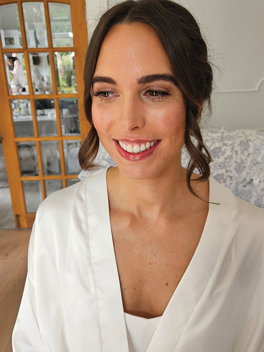 woman has her hair curled and swept out of her face, while wearing a white robe and smiling downwards