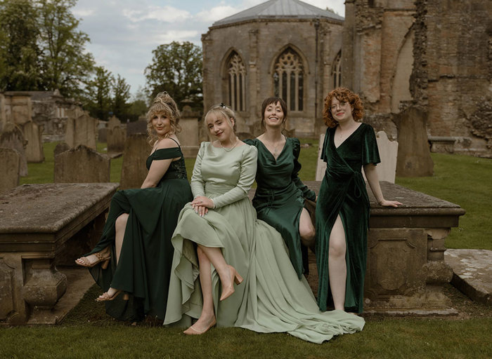 a bride wearing a pale green dress and three bridesmaids wearing dark green dresses posing on a stone tomb outside Elgin Cathedral