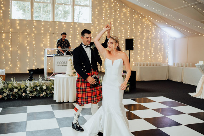 A bride and groom dancing in a room with a black and white chequered floor and fairylights.