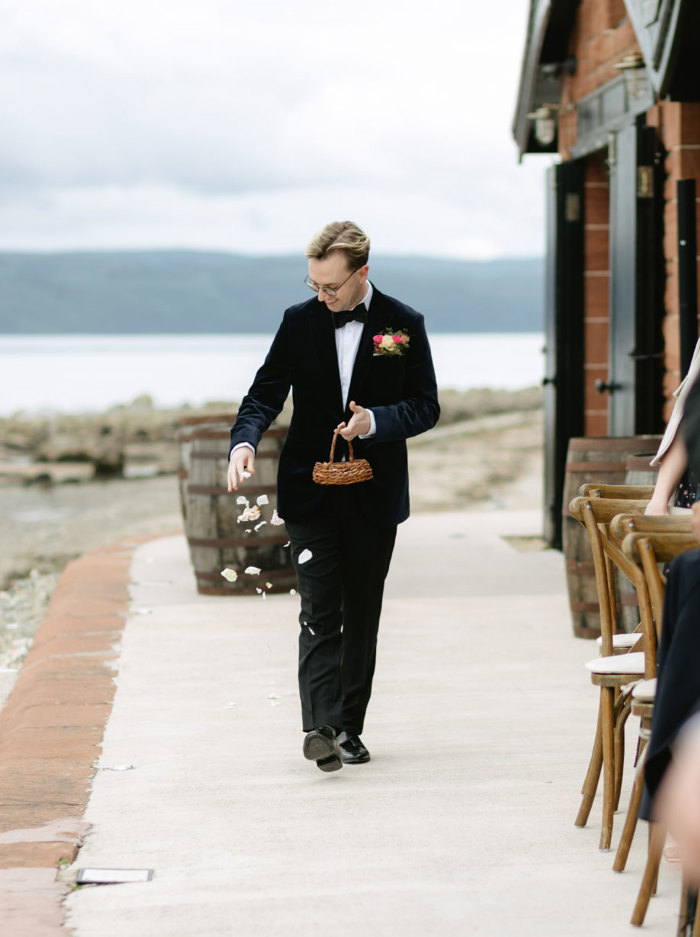 a man in a dinner suit sprinkling petals from a small wicker basket basket outside a building