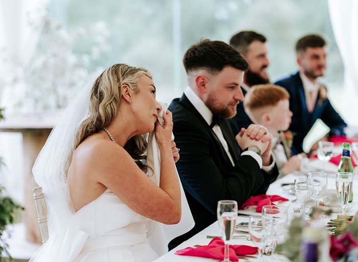 an emotional bride, sitting at a table at a wedding, dabbing away tears with a handkerchief 