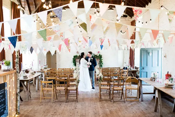 Bride holding bouquet and her groom smiling at each other in reception hall