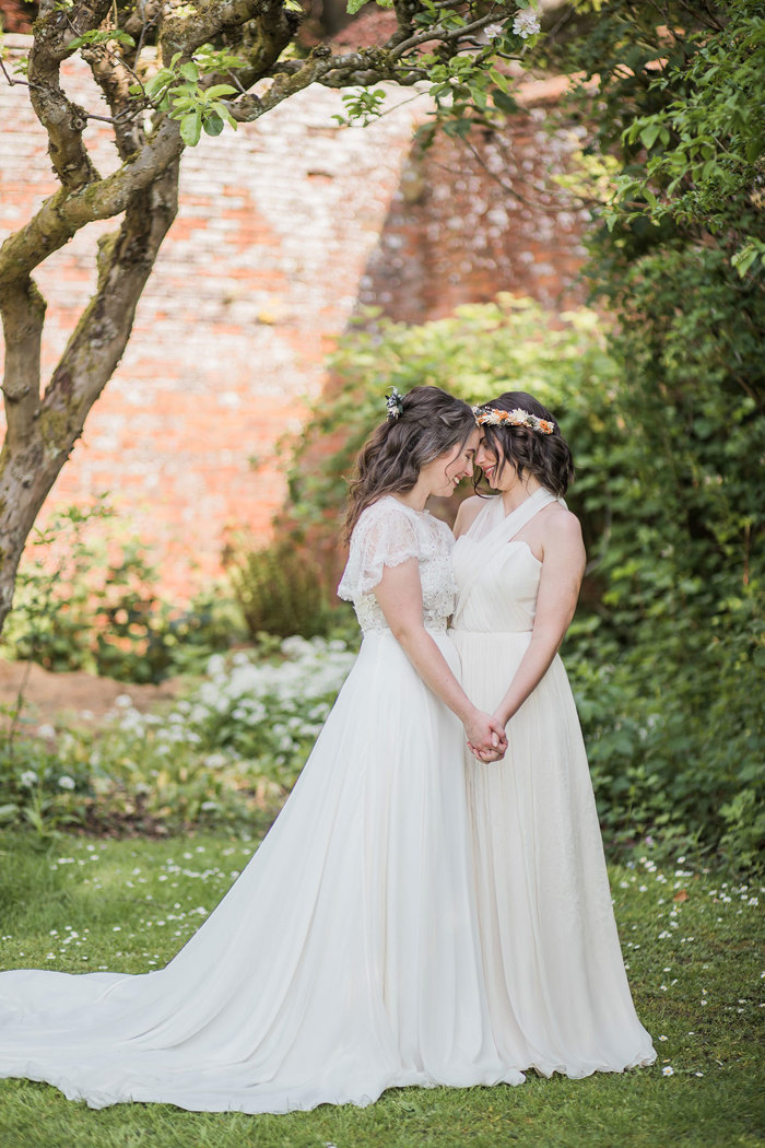 two brides wearing long and fluid wedding dresses standing romantically head-to-head in a walled garden setting at Byre at Inchyra