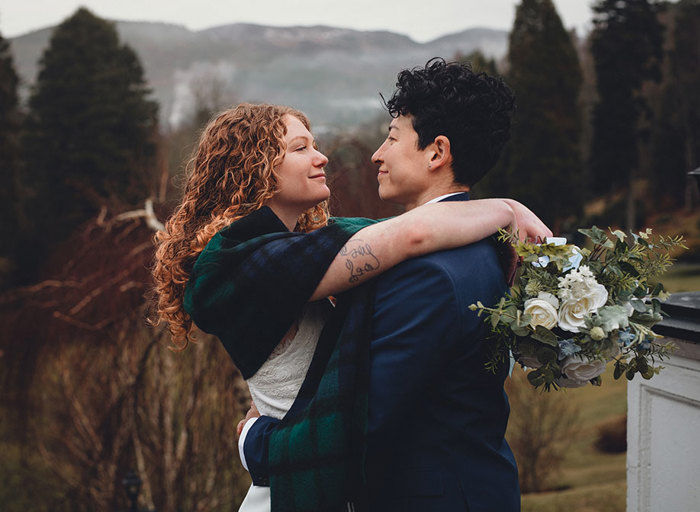 Two women look into each other's eyes with their arms around each other in a field