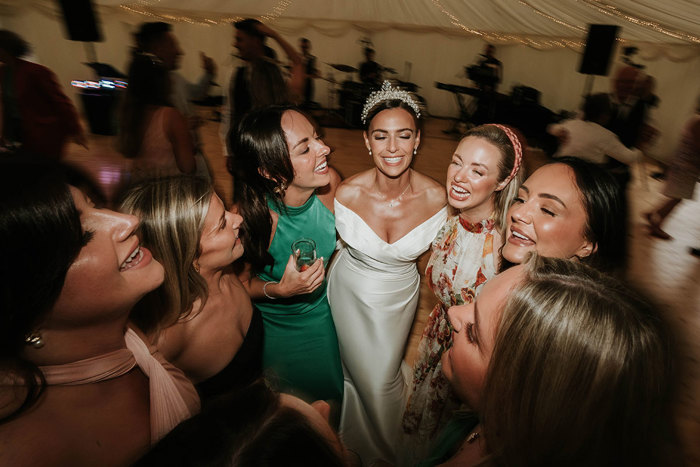 A group of woman smile while standing in a circle on a dancefloor and the background is blurred with motion