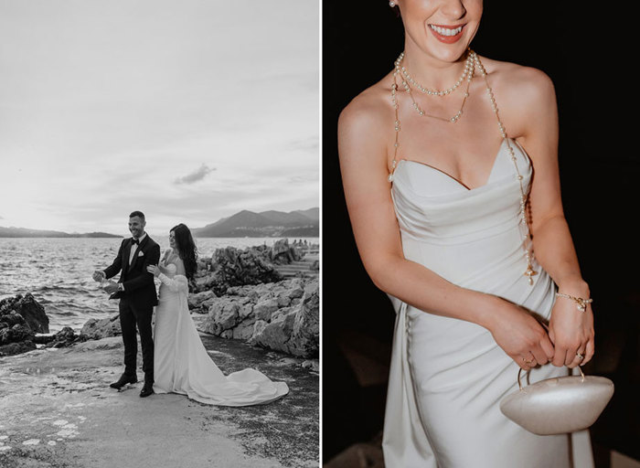 a groom opening bottle of champagne as bride stands behind him on rocky ground next to the sea on left. A bride wearing an ivory dress and long strands of pearls holding a small oval hard case bag