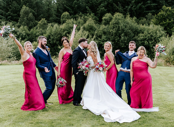 a bride and groom kissing with bridesmaids and groomsmen striking fun poses either side of them