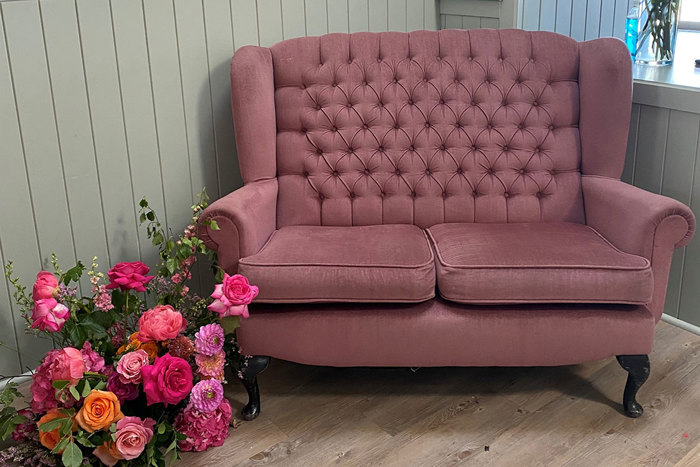 pink loveseat sofa with a bouquet of pink and orange flowers on the floor next to it