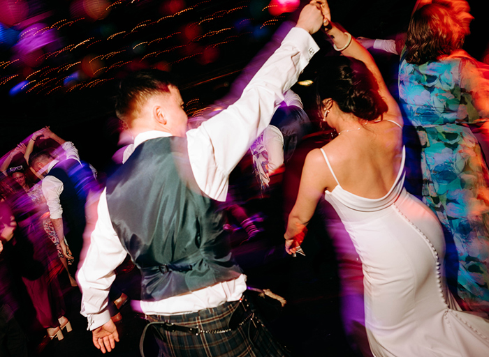 a man in a kilt spinning a bride wearing an ivory slip wedding dress under his arm as they dance