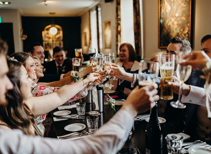 a group of people sitting around a long table reaching in with champagne glasses to toast cheers