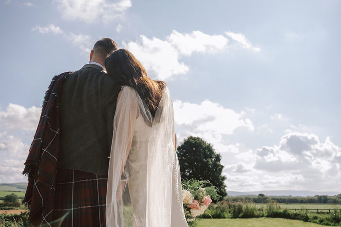 The backs of a couple resting their heads of each other and looking out at countryside views 