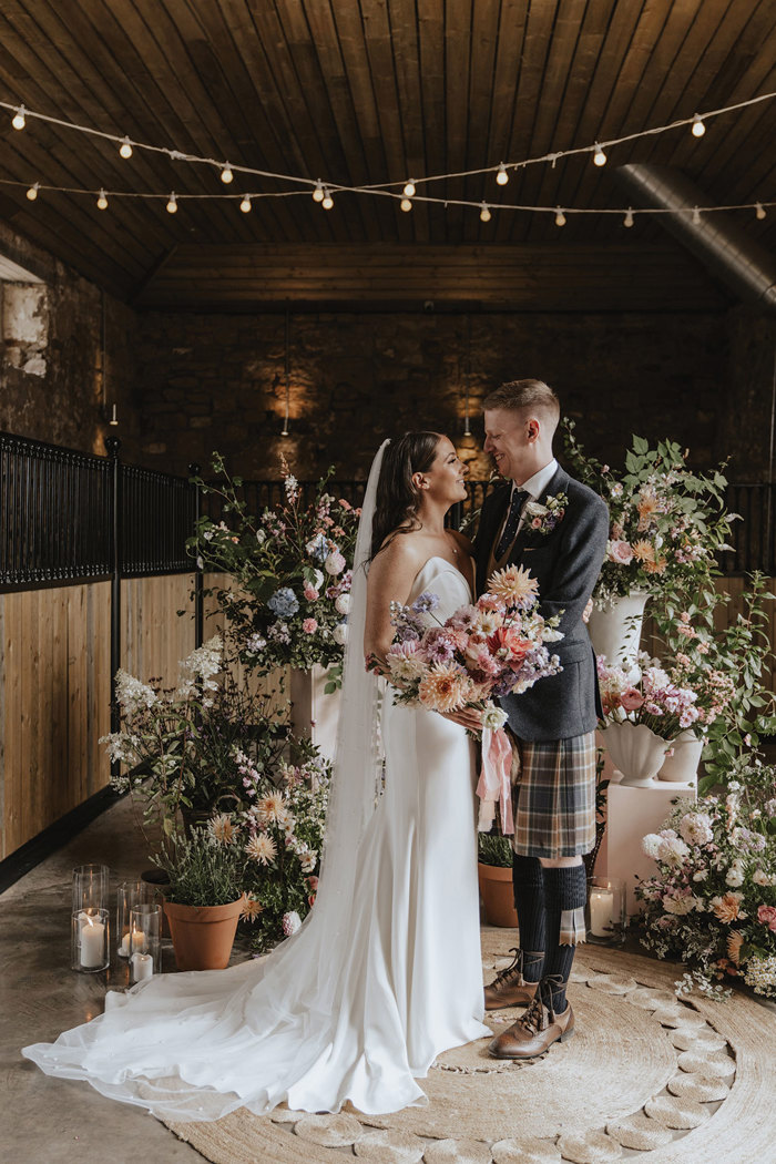 bride and groom smile at one another against a floral backdrop