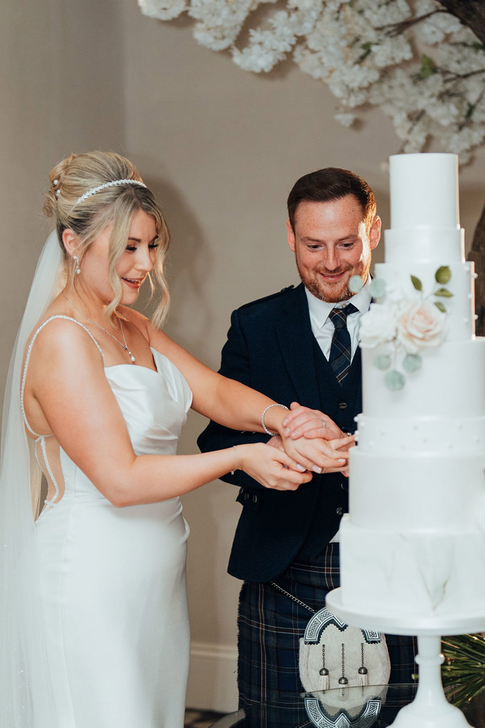 a smiling bride and groom cutting a tall five-tier wedding cake.