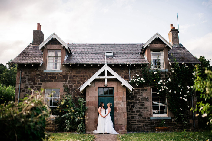 Brides hold hands outside brick building