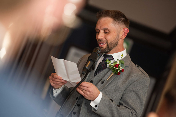 A Person Wearing A Grey Jacket And Buttonhole Reading From A Sheet Of Paper