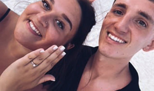 Two people taking a selfie, one of whom is showing off an engagement ring.