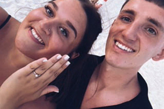 Two people taking a selfie, one of whom is showing off an engagement ring.