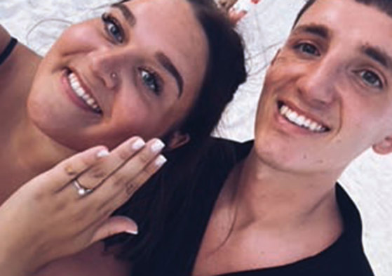 Two people taking a selfie, one of whom is showing off an engagement ring.