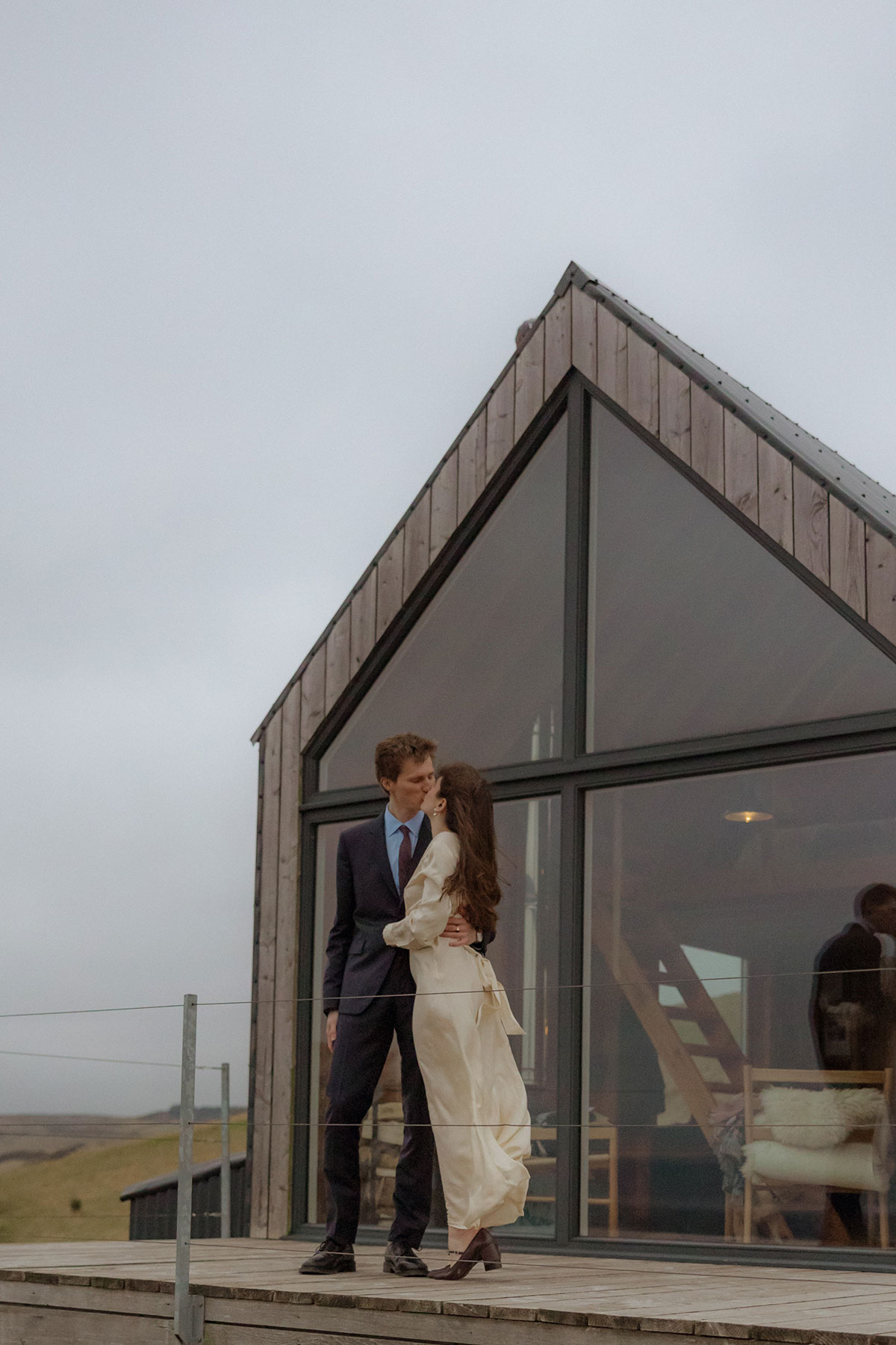 couple kiss in front of cabin with floor to ceiling windows