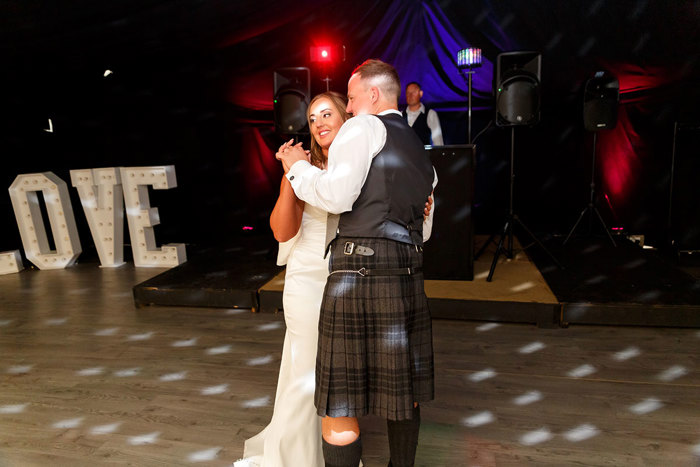 A bride and groom dancing together on a dancefloor under discoball reflections