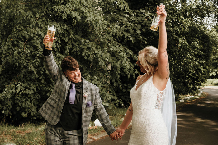 Brides hold hands and raise pints during couple portraits