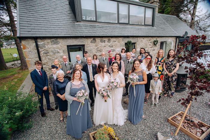 Two Brides, Bridesmaids And Wedding Guests Assembled Outside A House