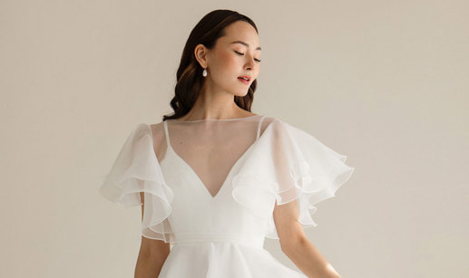dark haired model wears v-neck white wedding dress with sheer layer over bodice providing fluttery sleeves