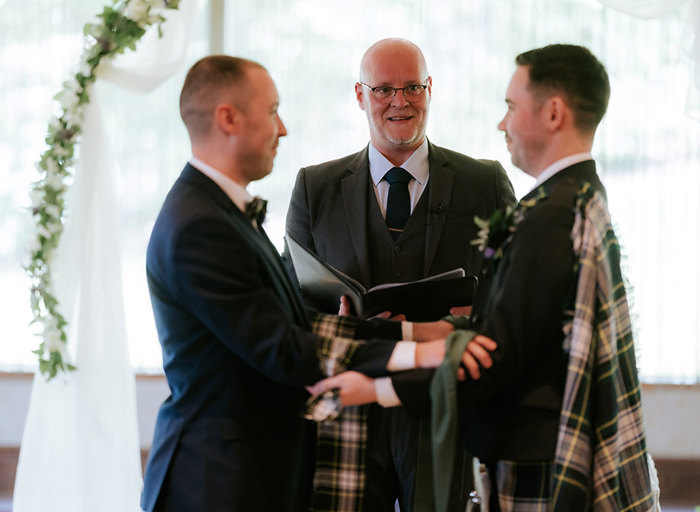 two grooms look at each other during wedding ceremony with celebrant in the background