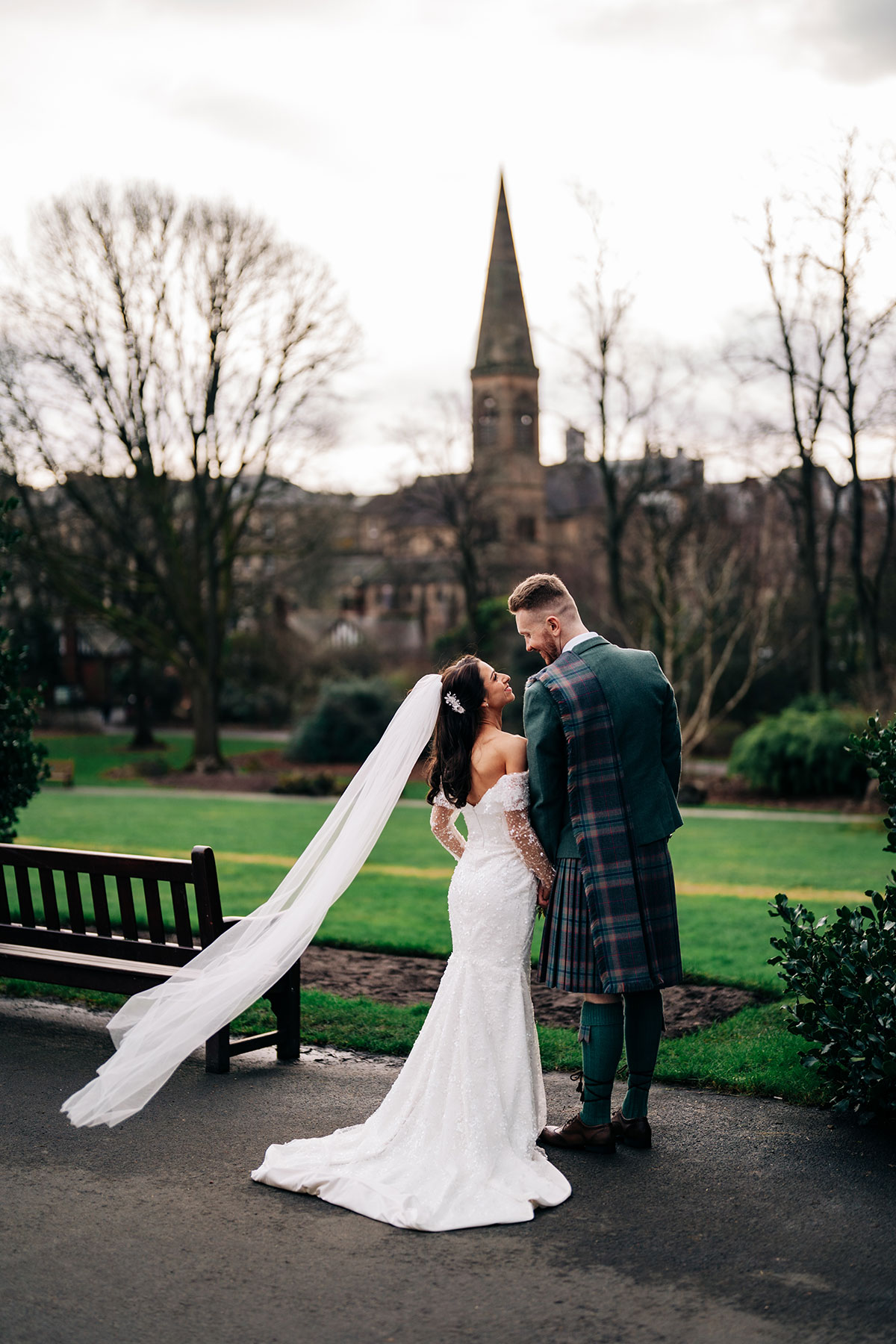 bride and groom smile at one another in glasgow botanic garden with oran mor out of focus in the background