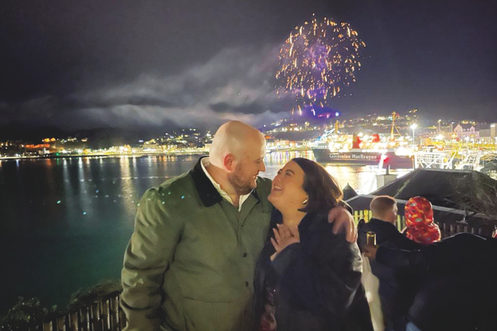 man and woman smiling at each other with water, ferry and fireworks in the background