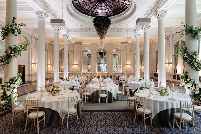 large dining space filled with round tables, tall columns and an impressive chandelier suspended in the middle