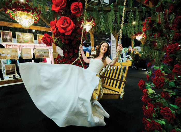 a model wearing a wedding dress on a large wooden chair swing that's surrounded by red rosese