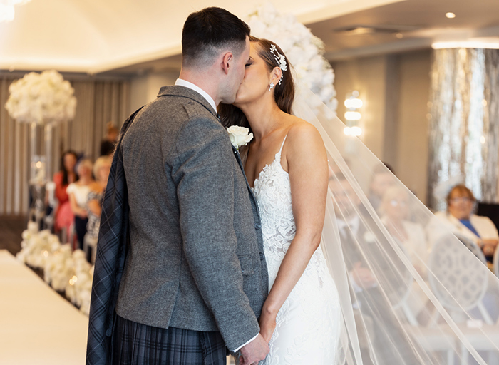 a newlywed bride and groom standing in front of guests. They are kissing and holding hands