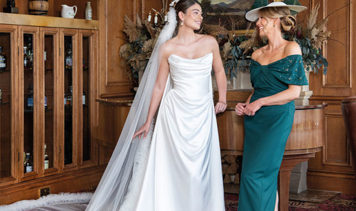 A bride wearing a strapless white wedding dress and long veil and a mother of the bride wearing forest green dress