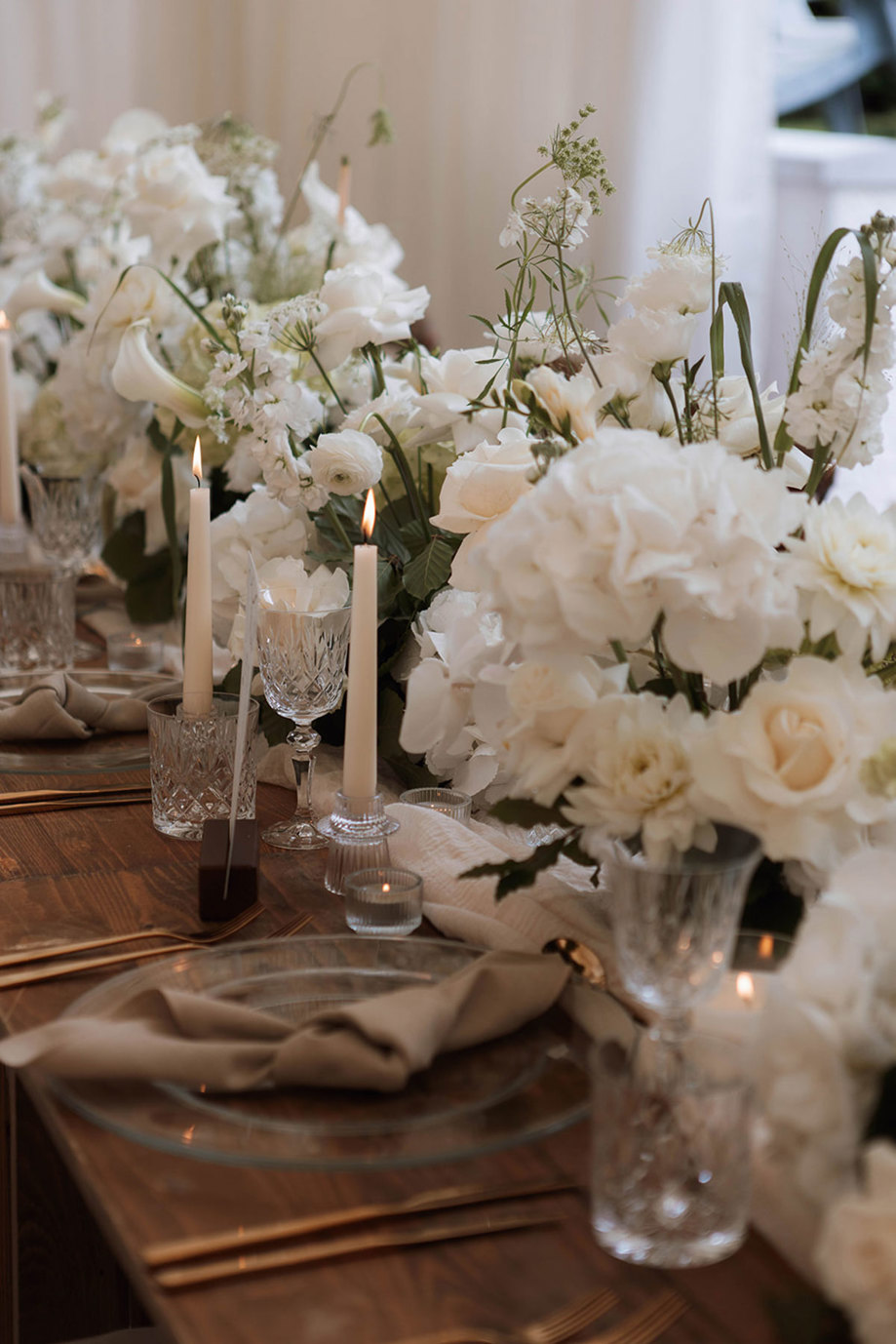 long table set with white flowers filling the centre and tall white candlesticks placed along the tableware