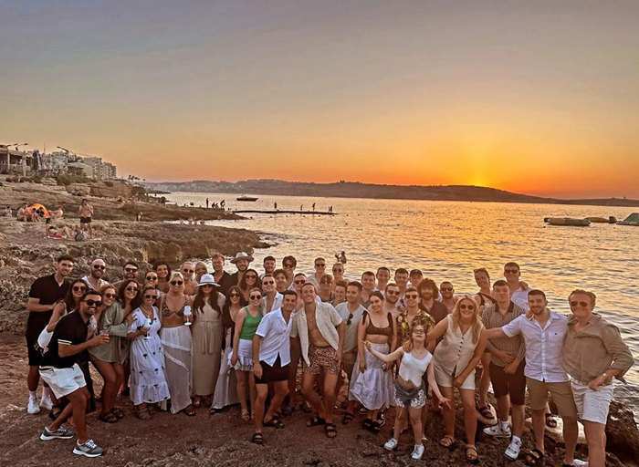 a group of people posing for a photo on a beach at sunset