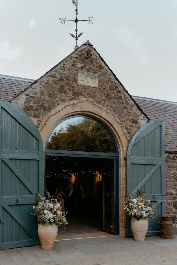 green wooden doors open and flower display in large urns at the Byre at Inchrya exterior