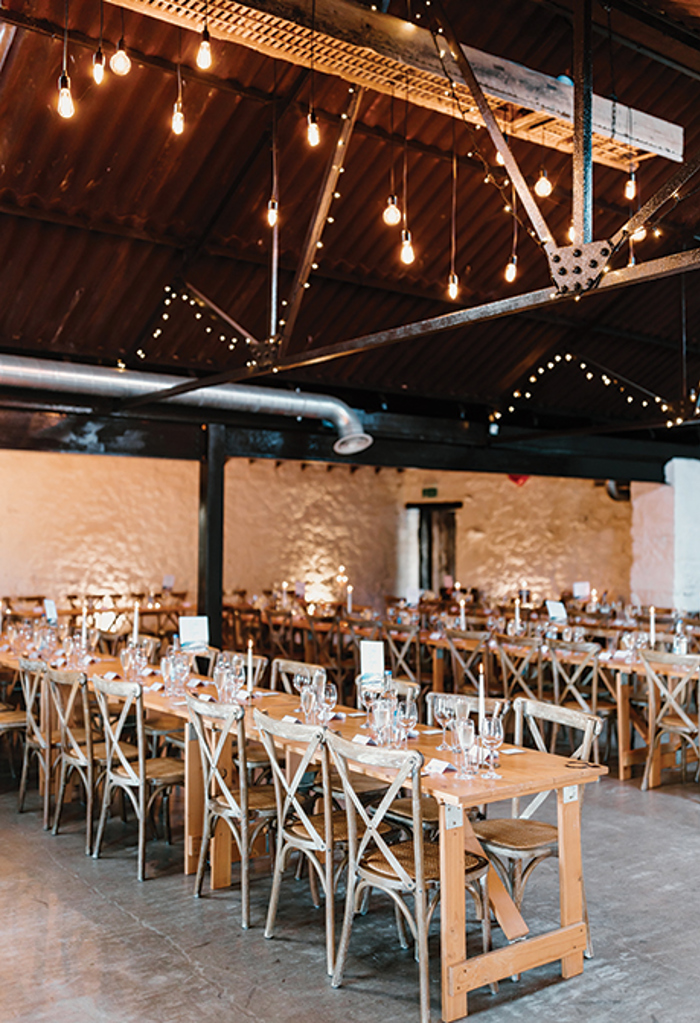 an indoor seating hall filled with long wooden tables, chairs and twinkly lighting fixtures hanging from the ceiling