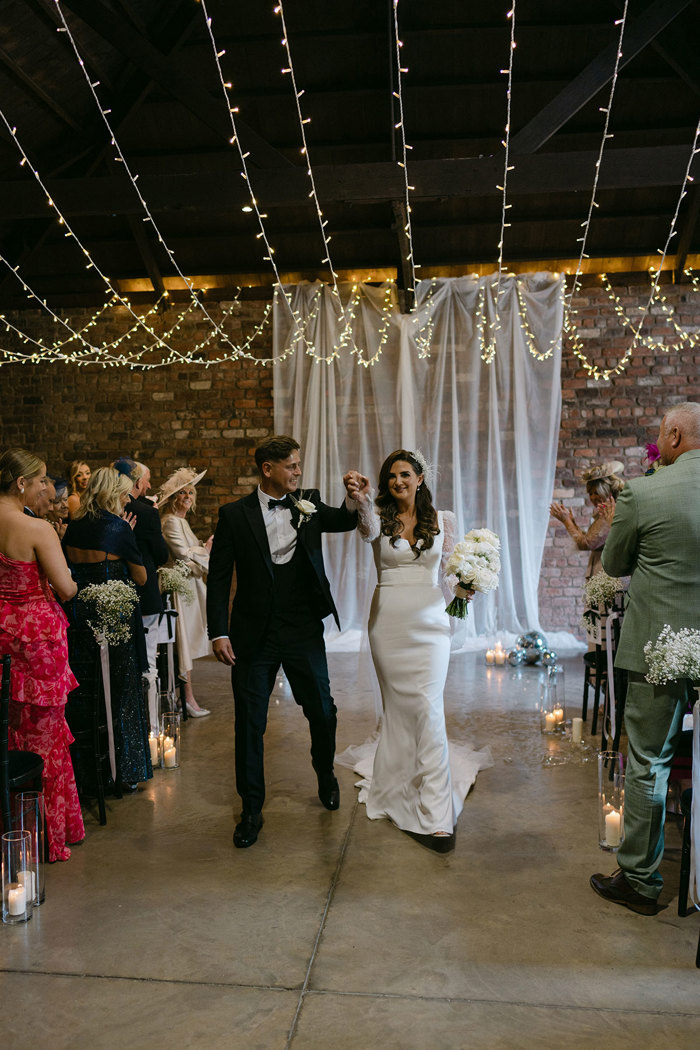 a bride and groom walking up the aisle between rows of seated guests at the Engine Works