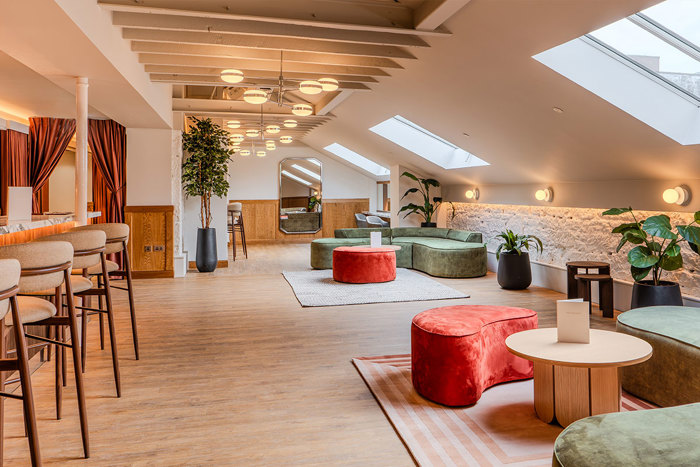 A room with wooden floors, sloping roofs, bar chairs on the left, and red and green couches on the right 