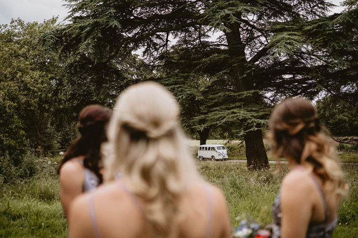 Bridesmaids watch the bride arrive in a VW Campervan