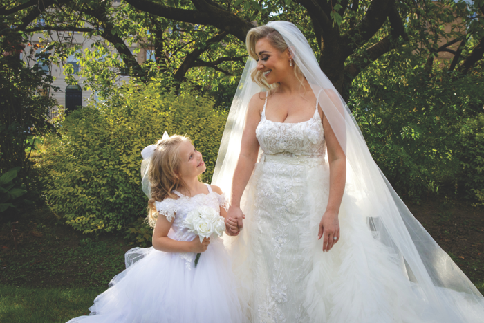 Bride and flower girl in white dresses looking at each other whilst holding hands