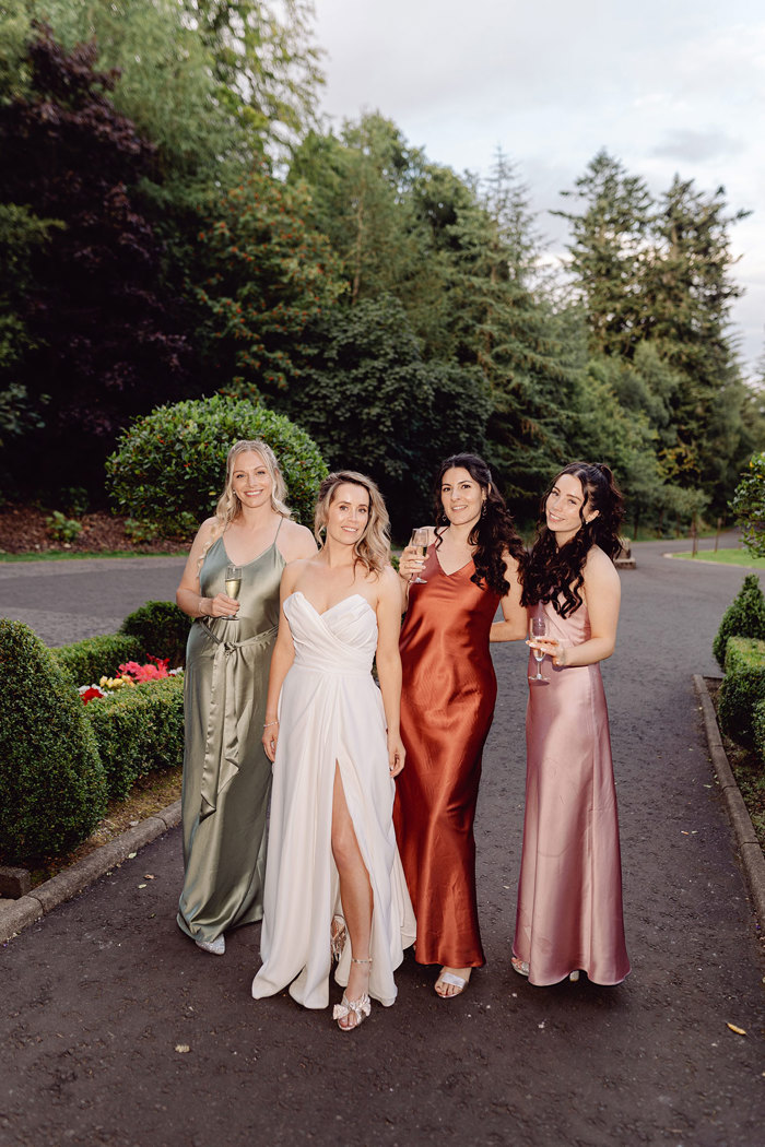 bride smiles with her bridesmaids who wear different coloured satin dresses