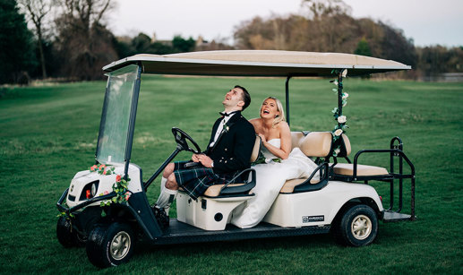 a laughing bride and groom on a golf buggy on a lawn