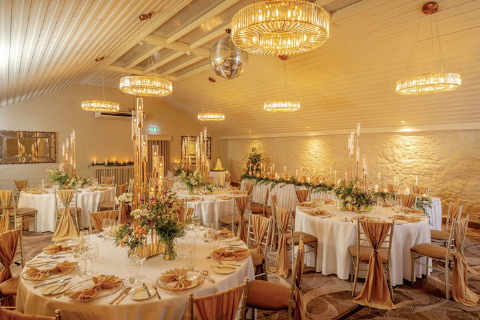 Round dining tables set up for a wedding reception with white table cloths and combinations of candles and floral centrepieces